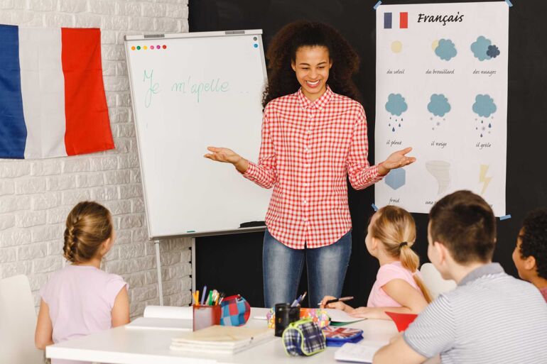Eine Lehrerin steht vor einem Flipchart und bringt Schülern Französisch bei. Vor ihr sitzen Schüler an einem Tisch.