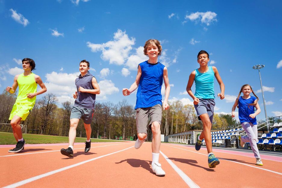 Fünf Schüler in Sportkleidung laufen auf einer Laufbahn auf einem Sportplatz.