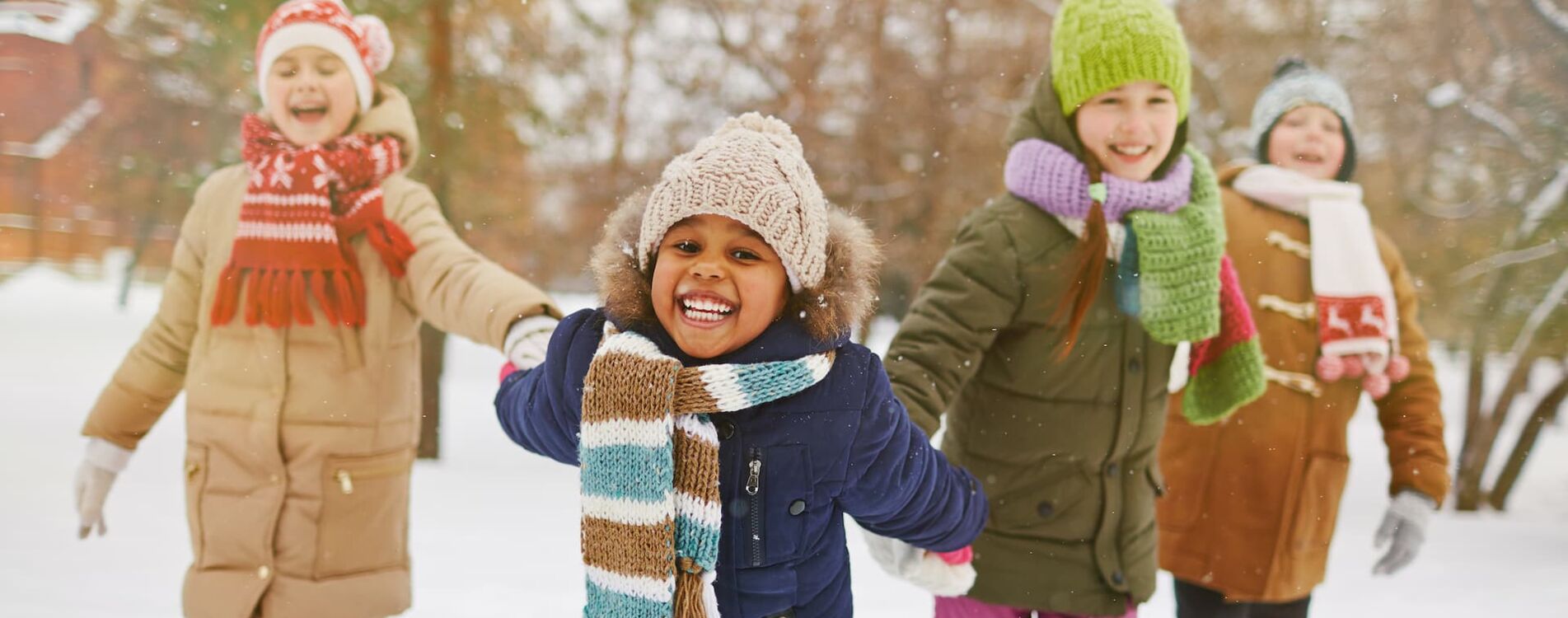 Winterspaß: Vier junge Mädchen in Winterkleidung draußen im Schnee fröhlich lachelnd halten sich an den Händen.