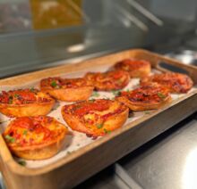 Eine Holzschale enthält mehrere kleine runde Pizzabrote (ähnlich Mini-Quiches oder Pizza-Muffins).