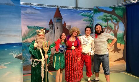 Fünf Schauspielerinnen und Schauspieler in bunten Kostümen stehen vor einem gemalten Schloss-Hintergrund.