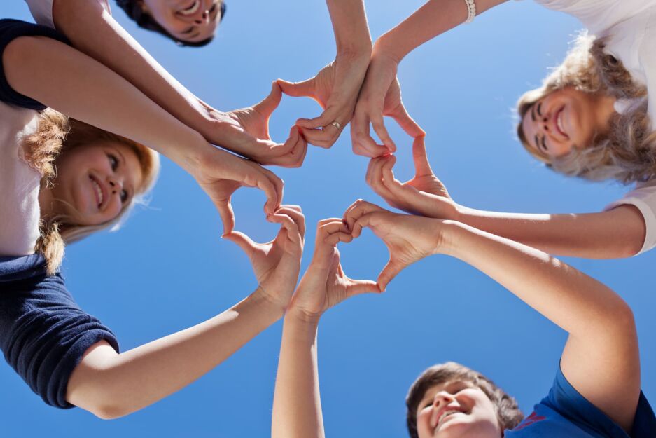 Perspektive von unten aus in den Himmel: Vier Teenager stehen im Kreis und bilden mit ihren Händen ein Herz.