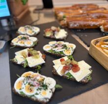 Belegte Vollkornbrote mit gekochten Eiern, Camembert, Radieschen, Trauben und frischen Kräutern, angerichtet auf einer schwarzen Schieferplatte