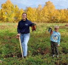 Frau und Kind ernten gemeinsam Karotten auf einem herbstlichen Feld, beide lächeln und halten frische Möhren in der Hand