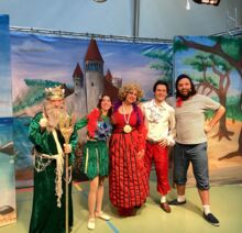 Fünf Schauspielerinnen und Schauspieler in bunten Kostümen stehen vor einem gemalten Schloss-Hintergrund.